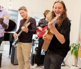 Musicians playing guitars in a bright indoor space, smiling and enjoying the jam session.